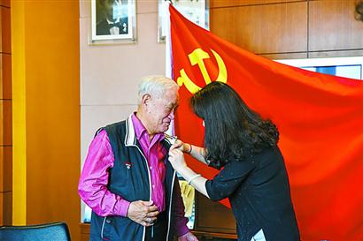 一位年轻党员为牛犇佩戴党徽。 